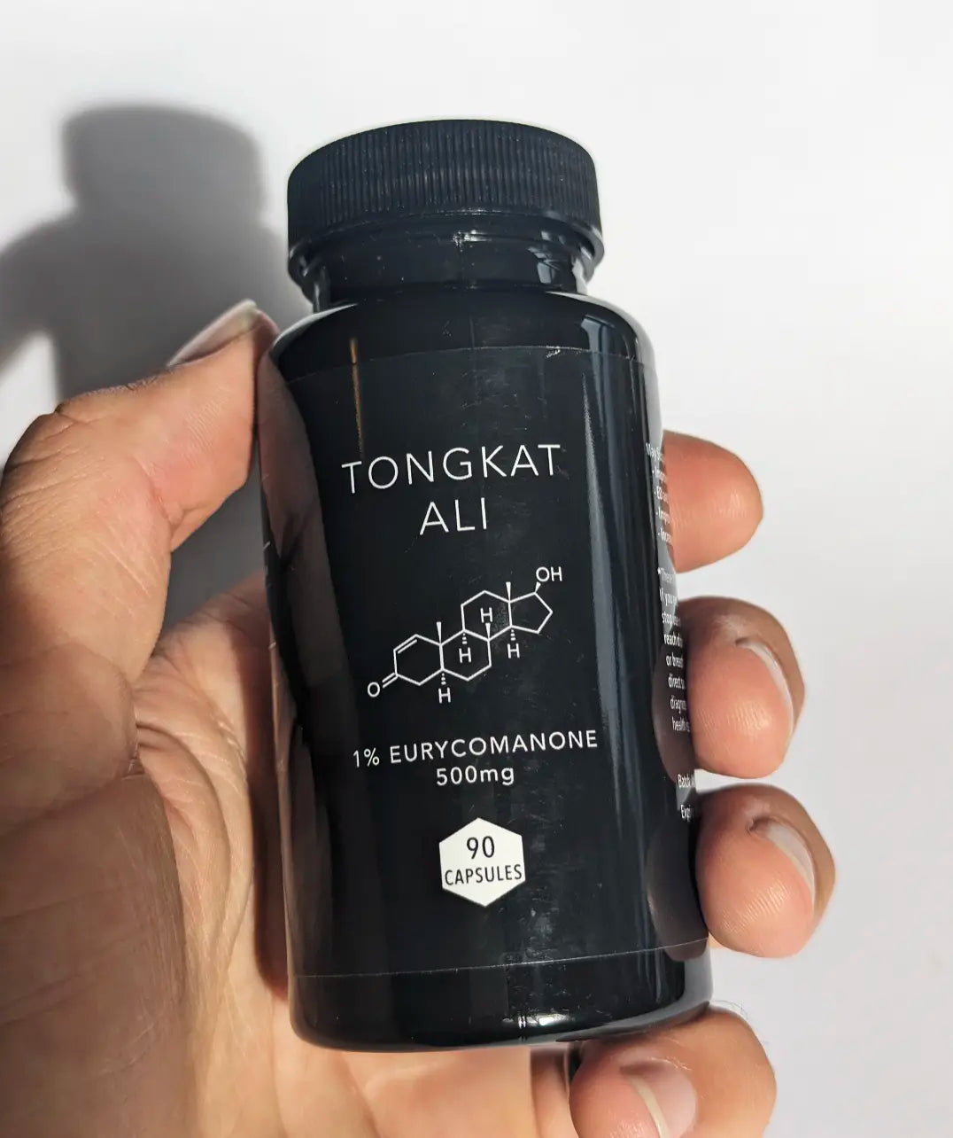 Hand holding a black bottle of Tongkat Ali with white text on a white background