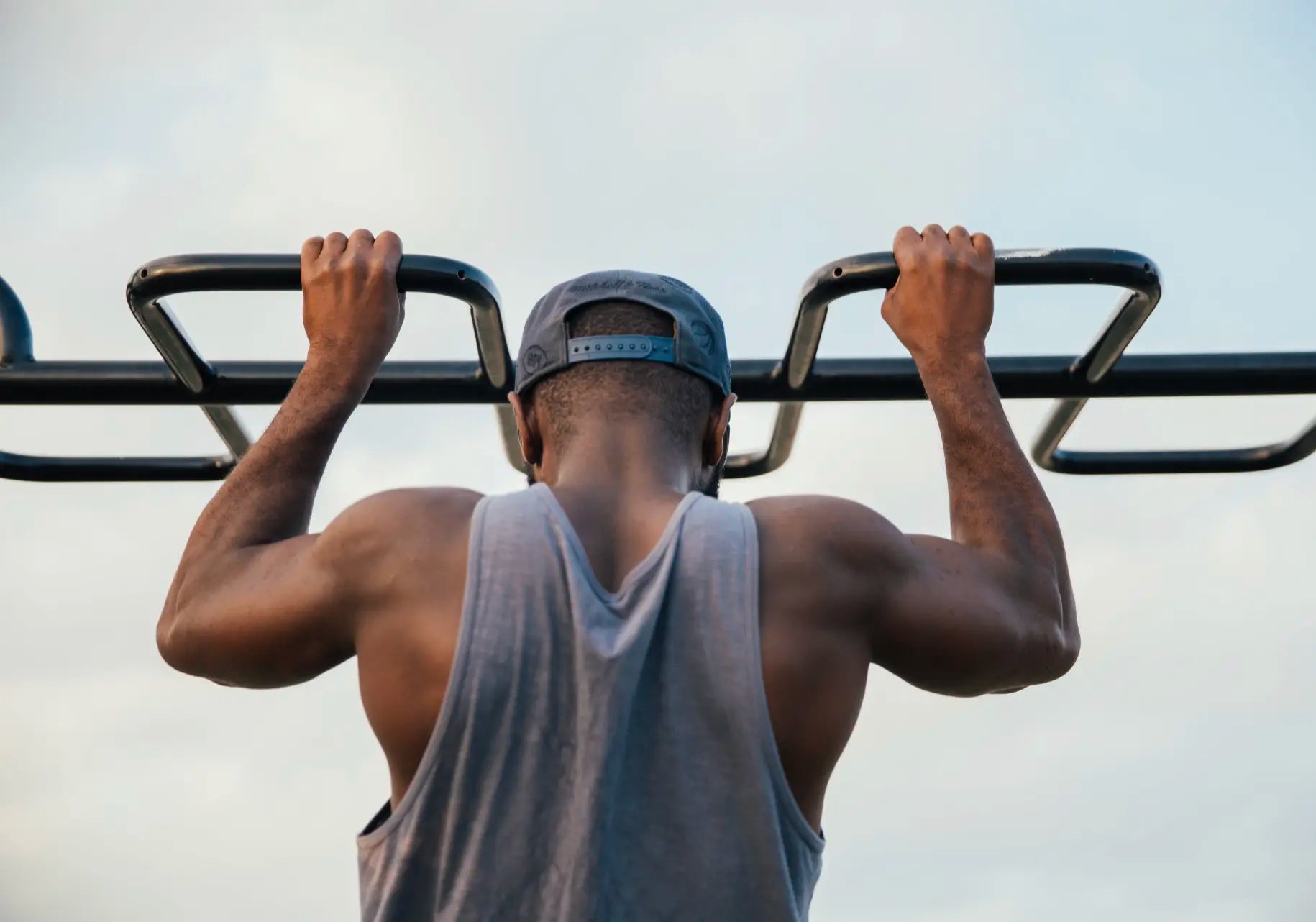 Person doing pull-ups on outdoor gym equipment with a clear sky background